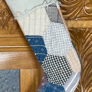 May include: A patchwork Christmas stocking with a white lace trim. The stocking is made of various fabrics in shades of blue, white, black, and beige.