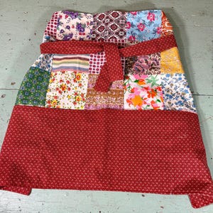 May include: A red patchwork skirt with a variety of floral and geometric patterns. The skirt has a wide red waistband and a gathered skirt.
