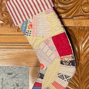 May include: A patchwork Christmas stocking with a red and white striped cuff. The stocking is made of various fabrics in shades of pink, yellow, blue, and red.
