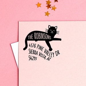 May include: A black cat silhouette with the text "The Robinsons" and their address "4576 Pine Valley Dr, Sierra Vista, AZ 54295" on a pink background with gold stars.