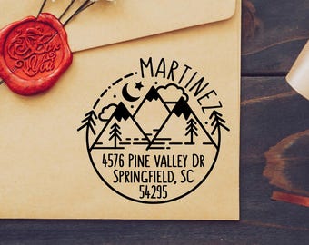 May include: A tan envelope with a red wax seal and a black address stamp. The stamp features a mountain and tree design with the name "Martinez" and an address. Dried flowers are attached to the envelope.