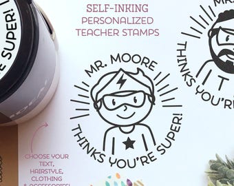 May include: Two self-inking teacher stamps with personalized designs. The stamps feature a superhero character with the text "Mr. Moore thinks you're super!" and a bearded man with the text "Mr. Thomas thinks you're super!"
