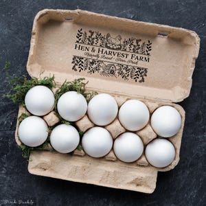 Custom rubber stamp impression reading "Hen & Harvest Farm – Naturally Raised · Farm Fresh" stamped in black ink on the inside lid of a green egg carton, shown with a dozen fresh brown eggs. Perfect for backyard chicken keepers, small farms, and handmade packaging.