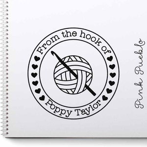May include: Black and white circular stamp with the text "From the hook of Poppy Taylor" and a yarn ball with a crochet hook. The text "Pink Pueblo" is written in cursive to the right of the stamp.