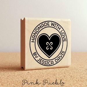 May include: A wooden stamp with a black circle design. The circle says "Handmade with Love by Jessica Davis" and has a black heart with an X in the center.