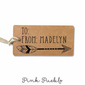 Peut inclure: Une étiquette cadeau en papier brun avec le texte "TO: FROM: MADELYN" et une flèche noire et blanche avec un motif de plume.