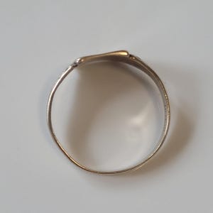 May include: A silver ring with a flattened top. The ring has a simple, elegant design, with a smooth, polished surface. The ring is likely made of metal and is shown against a neutral background.