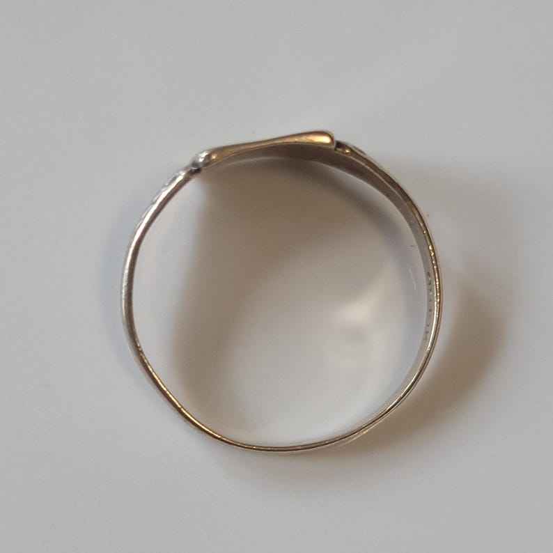 May include: A silver ring with a flattened top. The ring has a simple, elegant design, with a smooth, polished surface. The ring is likely made of metal and is shown against a neutral background.