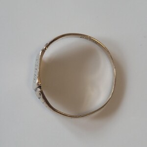 May include: A silver ring with a rectangular face and decorative detailing. The ring's band is thin and circular, and the face has etched designs. The ring is shown against a white background.