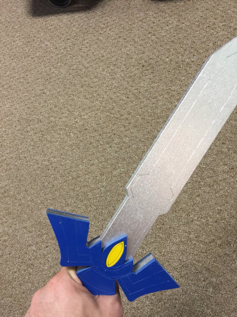 May include: A blue and silver toy sword with a yellow detail. The sword is made of foam and is held in a hand.