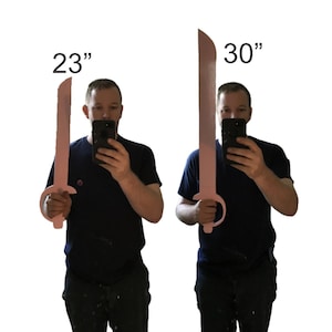 May include: Two pink toy swords, one 23 inches long and the other 30 inches long, are displayed. The swords have a curved blade design and a circular handle. The image is taken against a white background.