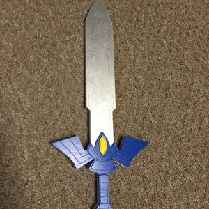 May include: A blue and silver toy sword with a yellow detail. The sword has a pointed tip and a handle with a blue and silver design.