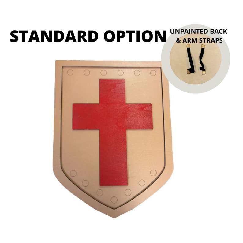 Puede incluir: Un escudo de madera con un dise&ntilde;o de cruz roja. El escudo tiene un borde marr&oacute;n claro con peque&ntilde;os detalles circulares. El texto "STANDARD OPTION" est&aacute; en la parte superior. Una incrustaci&oacute;n muestra la parte posterior sin pintar y las correas de los brazos.