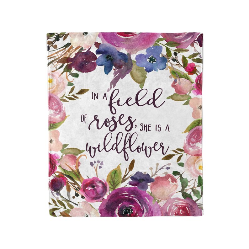 May include: A watercolor floral design with pink, purple, and blue flowers. The text "In a field of roses, she is a wildflower" is written in purple script.