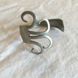 May include: A silver bracelet made from a repurposed fork, with the tines bent into a decorative design.