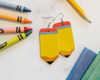 May include: A pair of yellow pencil-shaped earrings with red and gray accents. The earrings are made of wood and have a matte finish.