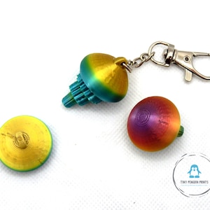 May include: Three colourful spinning tops, one with a silver keychain attached. The tops are yellow, blue, and green, red, orange, and purple.