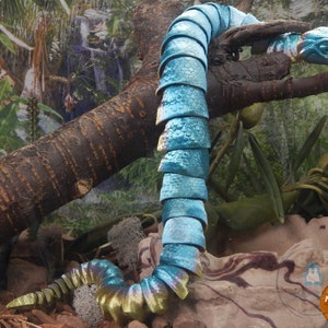 May include: A handcrafted, articulated snake sculpture with a turquoise and gold color scheme. The snake is posed on a tree branch, with a detailed head and segmented body. The sculpture is set against a backdrop of a jungle scene.