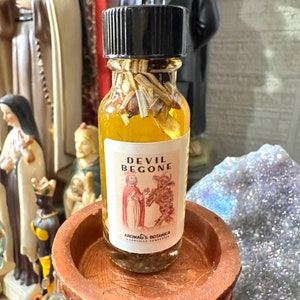 May include: A small glass bottle with a black cap filled with a yellow liquid and herbs. The label reads "Devil Begone" and "Aroma's Botanica Nashville Tennessee".