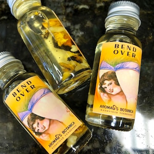 May include: Three glass bottles with labels that say "Bend Over" and "AromaG's Botanica Nashville Tennessee". The bottles contain a clear liquid and have a vintage aesthetic.