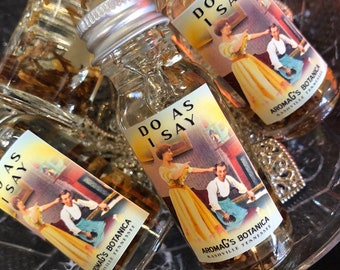 Könnte beinhalten: Vier kleine Glasflaschen mit Korkstopfen und Etiketten, auf denen "Do As I Say" und "Aromags's Botanica Nashville Tennessee" steht. Die Flaschen sind mit einer klaren Flüssigkeit gefüllt und haben ein Vintage-Design.