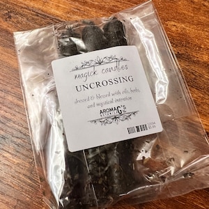 May include: A package of black magick candles labeled "Uncrossing" dressed and blessed with oils, herbs, and mystical intention. The label also includes the text "Magick Candles" and "AromaG's Botanica".