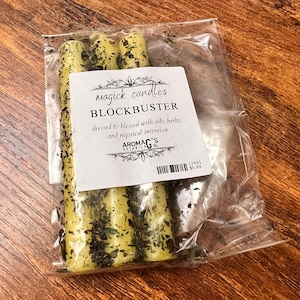 May include: Three yellow candles with green flecks, packaged in a clear plastic bag. The label reads "magick candles BLOCKBUSTER dressed & blessed with oils, herbs, and mystical intention AROMAG'S BOTANICA 12691 $5.99"