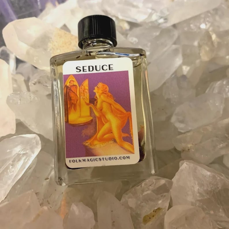 May include: A clear glass bottle with a black cap, labeled "SEDUCE" with a graphic of a woman. The bottle is surrounded by clear quartz crystals. The label also includes the website FOLKMAGICSTUDIO.COM.