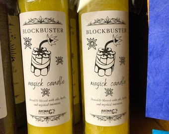May include: Two yellow candles with black and white labels. The labels say "Blockbuster magick candle" and feature a drawing of a lit stick of dynamite. The text on the label says "dressed & blessed with oils, herbs, and mystical intention" and "AromAG's Botanicals."