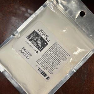 May include: A sealed, clear plastic bag containing white sachet powder. The bag has a label with the text "HOUSE BLESSING" and "SACHET POWDER". The label also includes a graphic of a house and trees, and text about the product's use in spells and rituals.