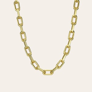 May include: A gold-colored chain necklace with elongated oval links. The necklace is displayed against a neutral background, highlighting its polished finish and simple design. The chain is a classic jewelry piece.