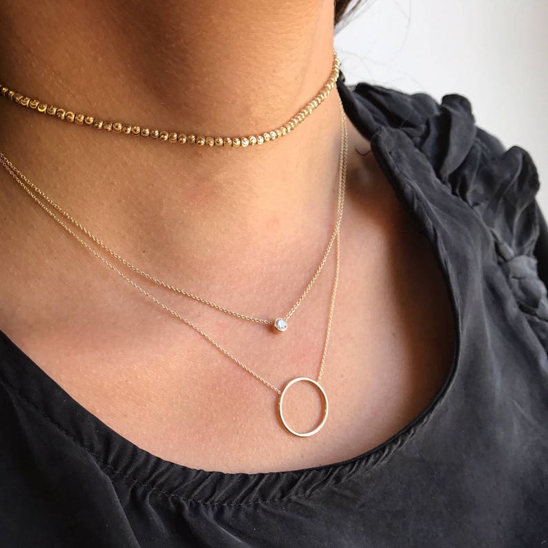 May include: A layered gold necklace set with a delicate chain, a small round pendant, and a larger circle pendant.