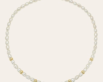 May include: A delicate necklace featuring oval-shaped white pearls interspersed with small gold-colored beads. The necklace has a gold-colored clasp and a small extender chain. The pearls are strung closely together, creating a classic and elegant look.