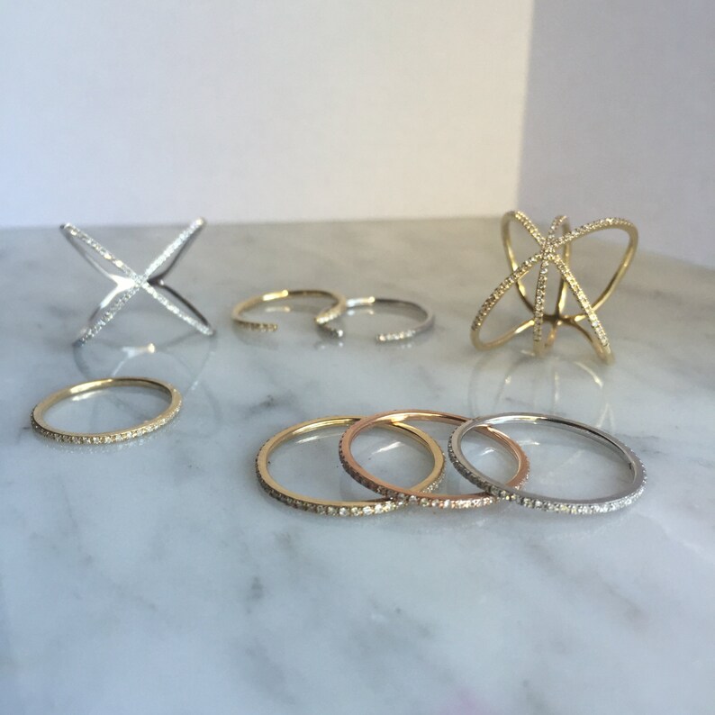 K&ouml;nnte beinhalten: Ein Set aus f&uuml;nf Diamantringen in verschiedenen Stilen. Die Ringe sind aus Gold und Silber und haben verschiedene Designs, darunter ein schlichtes Band, ein Kreuzdesign und ein filigraneres Design mit mehreren B&auml;ndern.