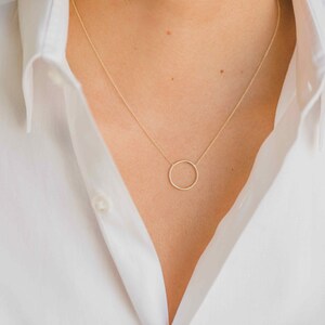 May include: A simple gold necklace with a delicate circle pendant.