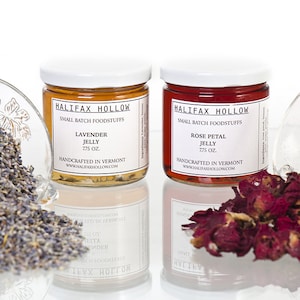 May include: Two jars of Halifax Hollow jelly with white lids, labeled "Lavender Jelly" and "Rose Petal Jelly", 275 oz each. Lavender and rose petals are in glass bowls on either side. The jars are handcrafted in Vermont.