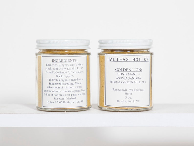 Puede incluir: Dos frascos de vidrio con tapas y etiquetas blancas. Una etiqueta enumera ingredientes como c&uacute;rcuma y jengibre. La otra etiqueta dice "Halifax Hollow Golden Lion: Lion's Mane + Ashwagandha Herbal Golden Milk Mix". Los frascos est&aacute;n llenos de un polvo dorado.