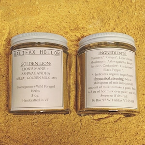 Puede incluir: Dos frascos de vidrio con tapas y etiquetas blancas, llenos de un polvo dorado, sobre una superficie amarilla. Las etiquetas dicen "HALIFAX HOLLOW" y "GOLDEN LION: LION'S MANE + ASHWAGANDHA HERBAL GOLDEN MILK MIX". Una etiqueta enumera los ingredientes.