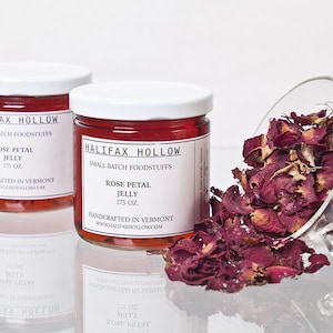 May include: Two glass jars of rose petal jelly with white lids, labeled "Halifax Hollow." A clear glass bowl tipped over, spilling dried rose petals. The jars are 2.75 oz each and handcrafted in Vermont.