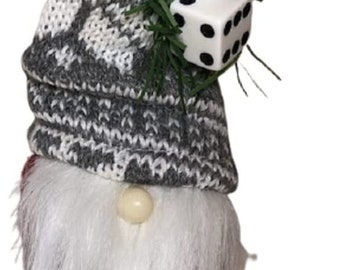 May include: A decorative gnome figurine featuring a tall, grey and white knit hat with a patterned design. The hat is adorned with two white dice with black pips and green artificial pine needles. The gnome has a long, white faux fur beard.