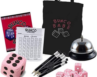 Può includere: Un set da gioco Bunco con una borsa tote nera che dice "Bunco Babe" in strass rosa, una campana argentata, dadi rosa, un foglio di punteggio, matite e un dado di peluche rosa.