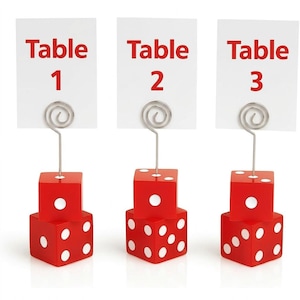 May include: Three red dice-shaped card holders with silver spiral wire clips. Each holder supports a white rectangular card printed with red text reading Table 1, Table 2, and Table 3 respectively. The dice feature white dots on their faces.