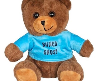 Puede incluir: Un oso de peluche marrón con ojos oscuros y un hocico de color marrón claro. El oso lleva una camiseta azul brillante de manga corta con el texto BUNCO GHOST impreso en letras negras en la parte delantera. Tiene almohadillas marrones claras.