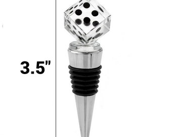Puede incluir: Un tapón para botella con un dado cúbico de acrílico transparente con puntos negros en la parte superior, unido a una base de metal plateado con anillos de goma negros. La altura total se indica como 3,5 pulgadas mediante una línea vertical.