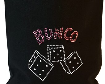 Op de afbeelding: Een zwarte draagtas met een strass-ontwerp op de voorzijde. Het ontwerp bevat het woord BUNCO in roze en rode strass-steentjes boven drie witte strass-dobbelstenen. De tas heeft twee zwarte stoffen handvatten aan de bovenkant om te dragen.