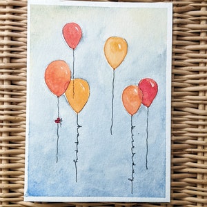 Puede incluir: Pintura acuarela de una tarjeta de cumpleaños con globos naranja, rojo y amarillo. Los globos tienen cuerdas que deletrean "feliz cumpleaños".