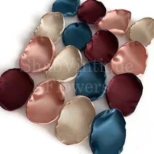 May include: Assortment of silk flower petals in burgundy, blush pink, cream, and teal colors. The petals are arranged on a white surface.