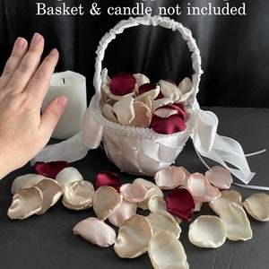 Puede incluir: Una colecci&oacute;n de p&eacute;talos de flores artificiales en tonos burdeos, crema y rosa suave. El texto en la imagen dice: Example shown approx. 100 petals. Basket & candle not included. Estos p&eacute;talos de tela est&aacute;n esparcidos sobre una superficie.