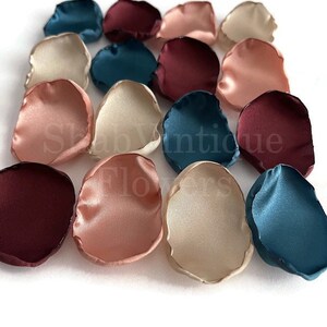 May include: A collection of silk flower petals in shades of burgundy, teal, and blush. The petals are arranged in a random pattern on a white background.