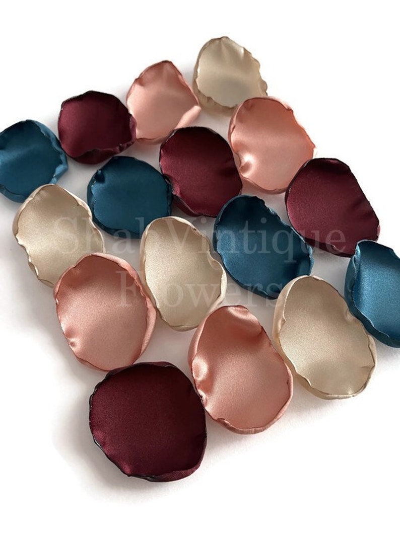 May include: Assortment of silk flower petals in burgundy, teal, blush pink, and cream colors. The petals are arranged in a scattered pattern on a white background.